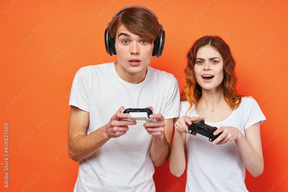 young couple in white t-shirts with joysticks playing a console orange background young couple in white t-shirts with joysticks playing a console orange background