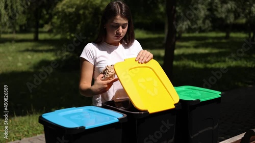 Middle selection of female hold two different type of rubbish, plastic container and paper and thowing into different recycling bins. Close-up of woman stand by blue, yeallow and green bin photo