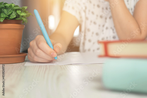 Woman writing on paper, concept of home education, wooden table with notebooks