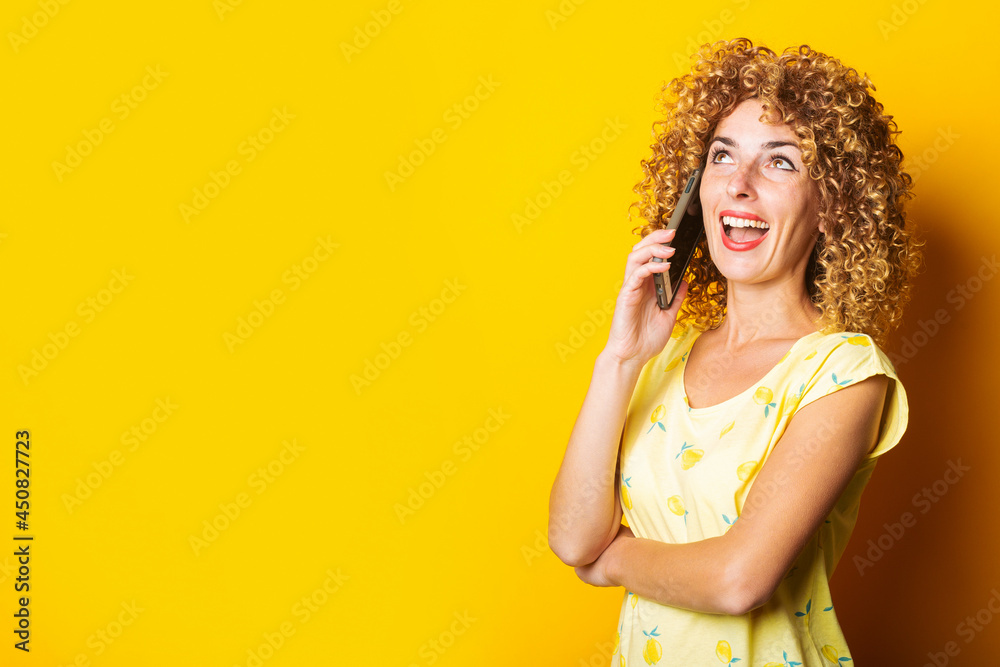 curly young woman talking on the phone on a yellow background. curly young woman talking on the phone on a yellow background.