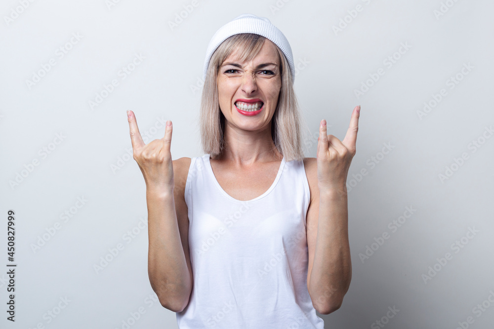Young blonde woman shows rocker horns on a light background Young blonde woman shows rocker horns on a light background