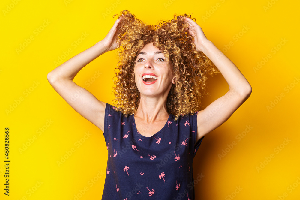 cheerful curly young woman lifts her hair up on a yellow background cheerful curly young woman lifts her hair up on a yellow background