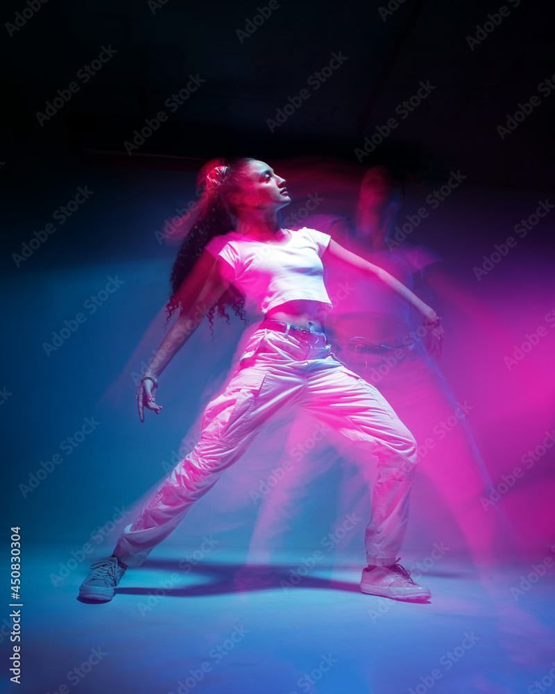Dancing mixed race young girl in colourful neon studio light. Female dancer in white stylish sportswear. Long exposure