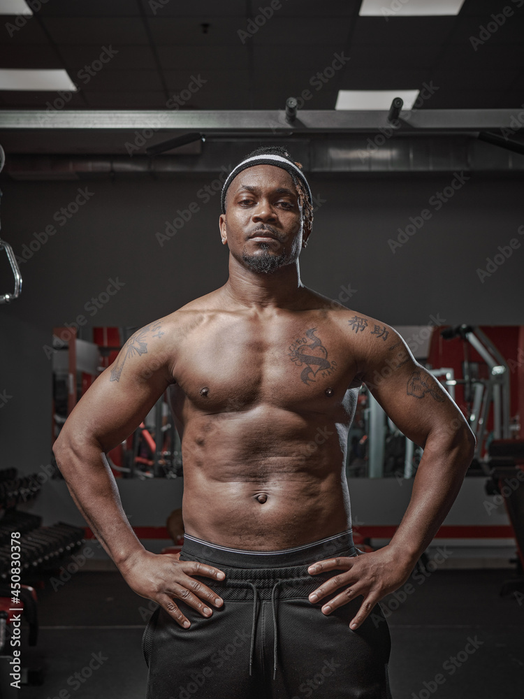 Brutal muscular athletic african american guy with naked torso posing on training in gym. Visceral fat on belly