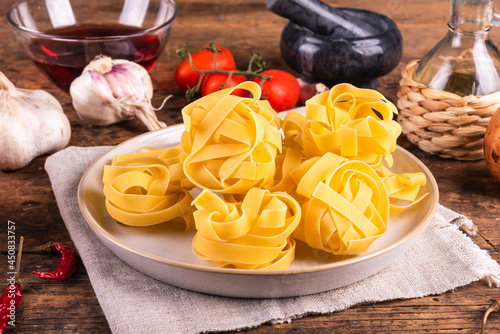 Raw fettuccine pasta in a plate, tomatoes, garlic and peppers, olive oil, wine on the table. Family dinner ingredients, close-up.