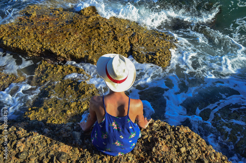 Beautiful young woman in a dress sitting by the sea in Spain.