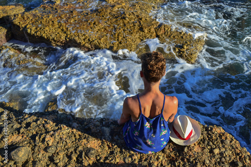 Beautiful young woman in a dress sitting by the sea in Spain.