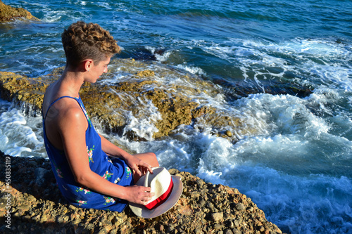 Beautiful young woman in a dress sitting by the sea in Spain.
