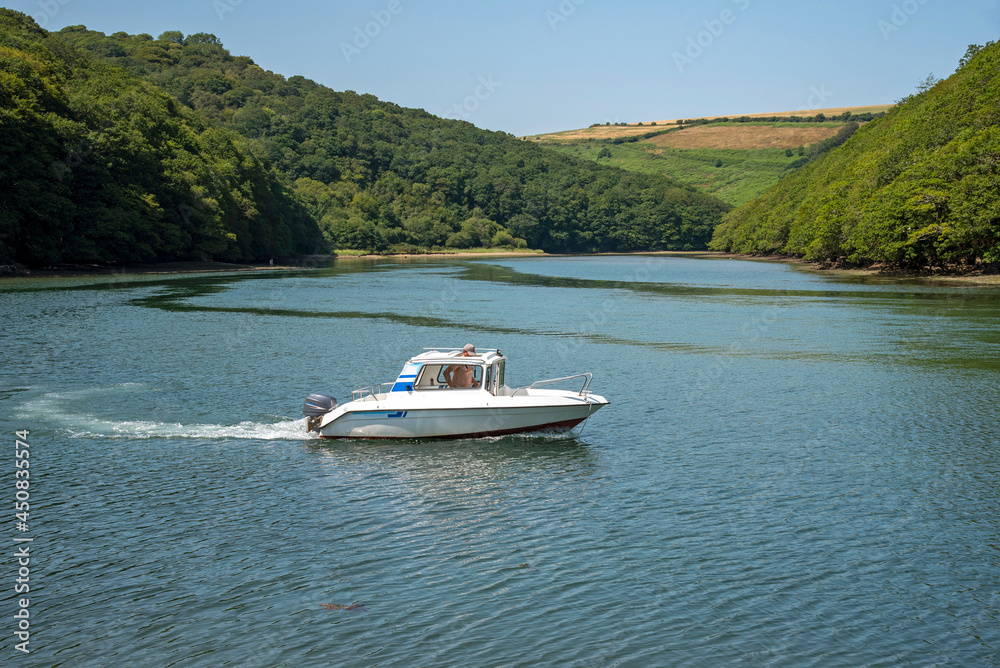 Obraz premium Looe, Cornwall, England, UK. 2021. A small cabin cruiser on the River Looe with a backdrop of Cornish countryside.