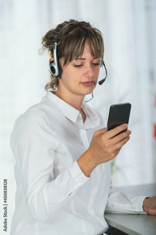 Portrait of a woman customer support call operator in office using mobile phone Portrait of a woman customer support call operator in office using mobile phone