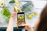Young woman takes photo of half of avocado in her hand