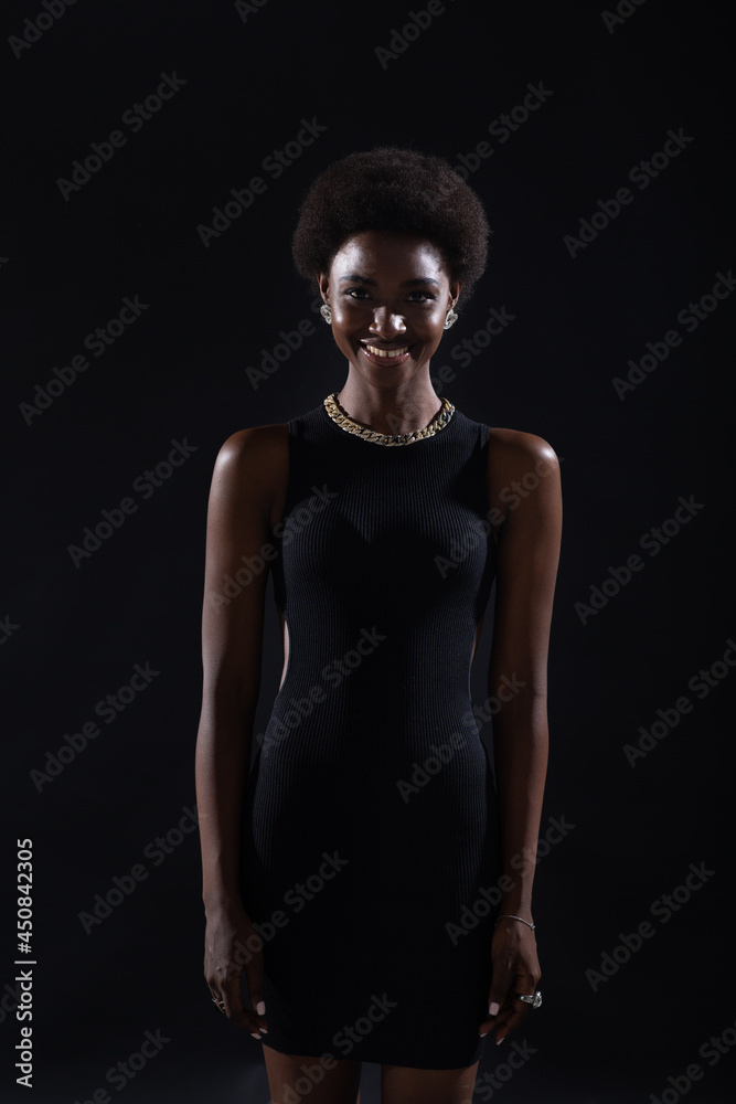 Naklejka premium Standing smiling portrait of african american woman with afro hairstyle on black studio background.