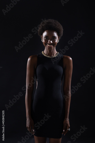 Standing smiling portrait of african american woman with afro hairstyle on black studio background.