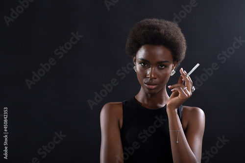 Pretty model african american woman smoking cigarette on black background.