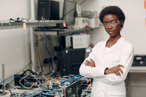 Fotografiet Scientist african american woman standing and looking at camera in laboratory with electronic tech single photon decoder encoder