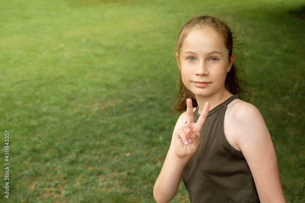 Young smiling teenager girl showing peace sign on green, outdoor park background Young smiling teenager girl showing peace sign on green, outdoor park background