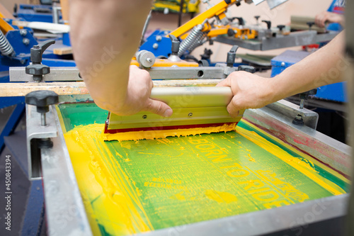 Serigraphy silk screen print process at clothes factory. Frame, squeegee and plastisol color paints.