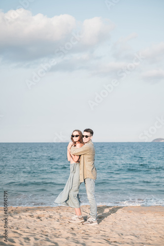 Couple in love standing on the beach and cuddling. Wearing sunglasses and casual clothes. Seaview. High quality photo © Aleksandr