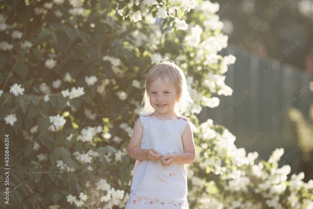 the blonde baby is smiling, her hair is illuminated by the setting sun, and sand is falling from her hands