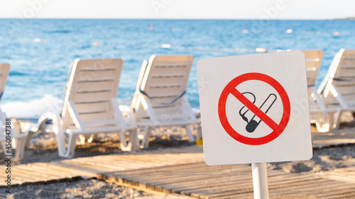 Fototapeta Naklejka Na Ścianę i Meble -  No smoking sign on the beach in summer. There are sun loungers on the background.