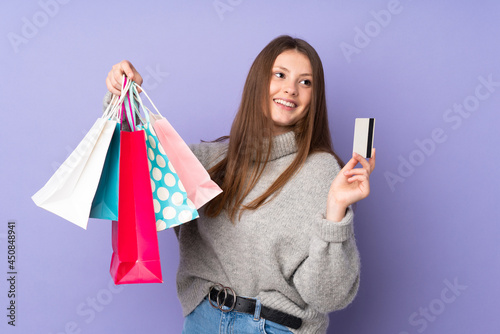 Teenager caucasian girl isolated on purple background holding shopping bags and a credit card