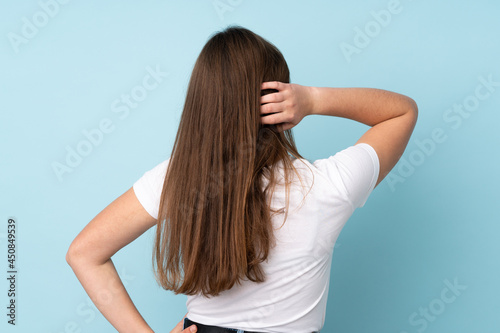 Teenager caucasian girl isolated on blue background in back position and thinking