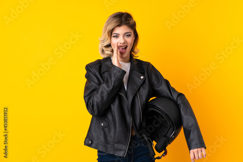 Teenager woman holding a motorcycle helmet isolated on yellow background shouting with mouth wide open