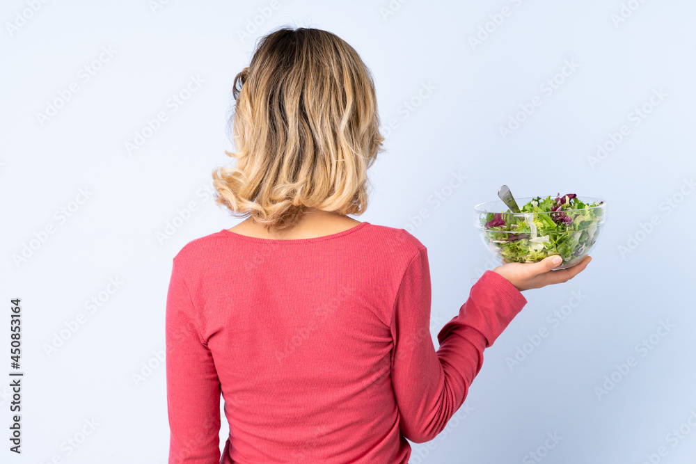 Teenager woman with salad isolated on blue background in back position Teenager woman with salad isolated on blue background in back position