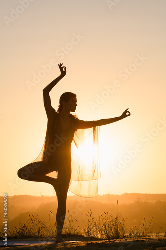 Female silhouette in yoga tree balance pose and mudra hands triange, dancing , fitness training outdoors in warm sun light