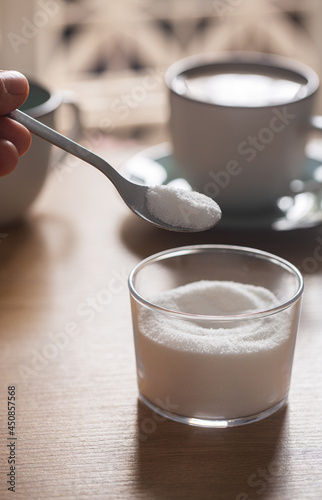 Hand holds spoon with sweetener on coffee background photo