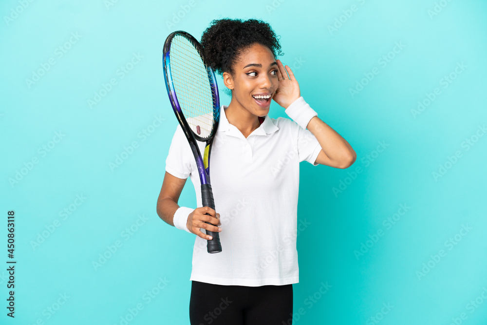 Young tennis player woman isolated on blue background listening to something by putting hand on the ear Young tennis player woman isolated on blue background listening to something by putting hand on the ear