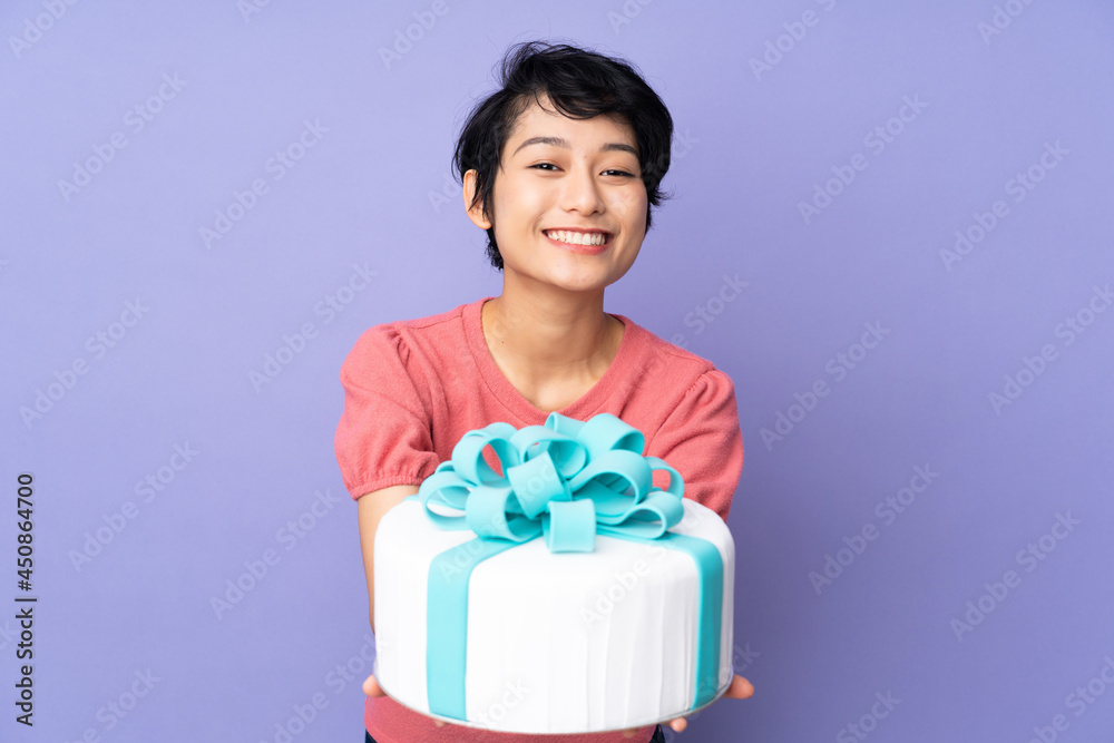 Young Vietnamese woman with short hair holding a big cake over isolated purple background Young Vietnamese woman with short hair holding a big cake over isolated purple background