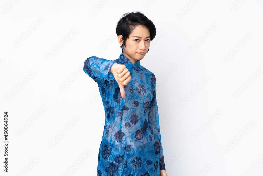 Young Vietnamese woman with short hair wearing a traditional dress over isolated white background showing thumb down with negative expression Young Vietnamese woman with short hair wearing a traditional dress over isolated white background showing thumb down with negative expression