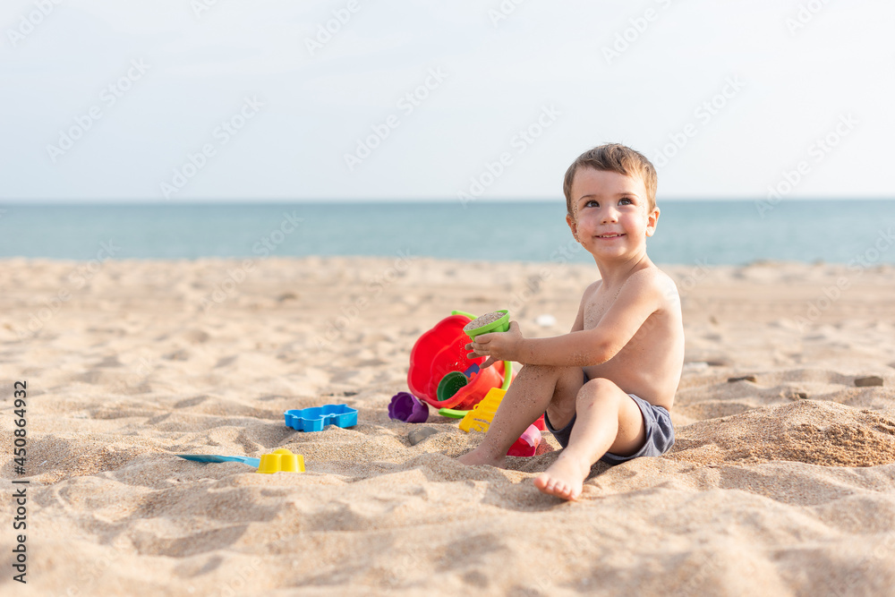 Adorable kid plays on the seashore in the sand with toys. Summer holidays Adorable kid plays on the seashore in the sand with toys. Summer holidays