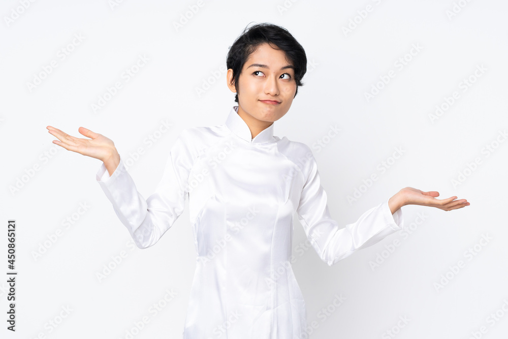 Young Vietnamese woman with short hair wearing a traditional dress over isolated white background making doubts gesture Young Vietnamese woman with short hair wearing a traditional dress over isolated white background making doubts gesture