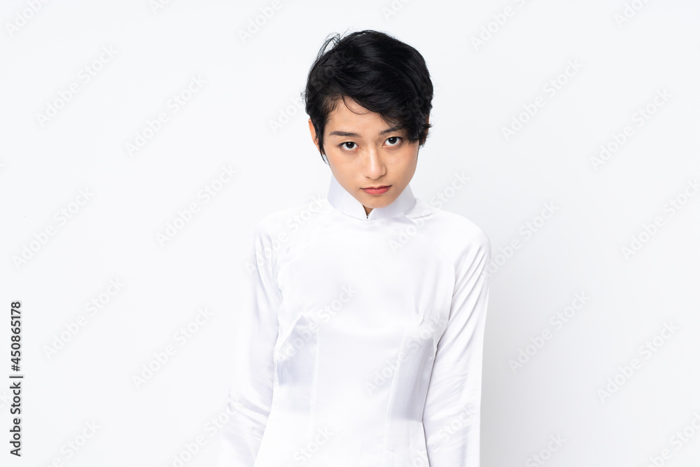 Young Vietnamese woman with short hair wearing a traditional dress over isolated white background with sad expression Young Vietnamese woman with short hair wearing a traditional dress over isolated white background with sad expression