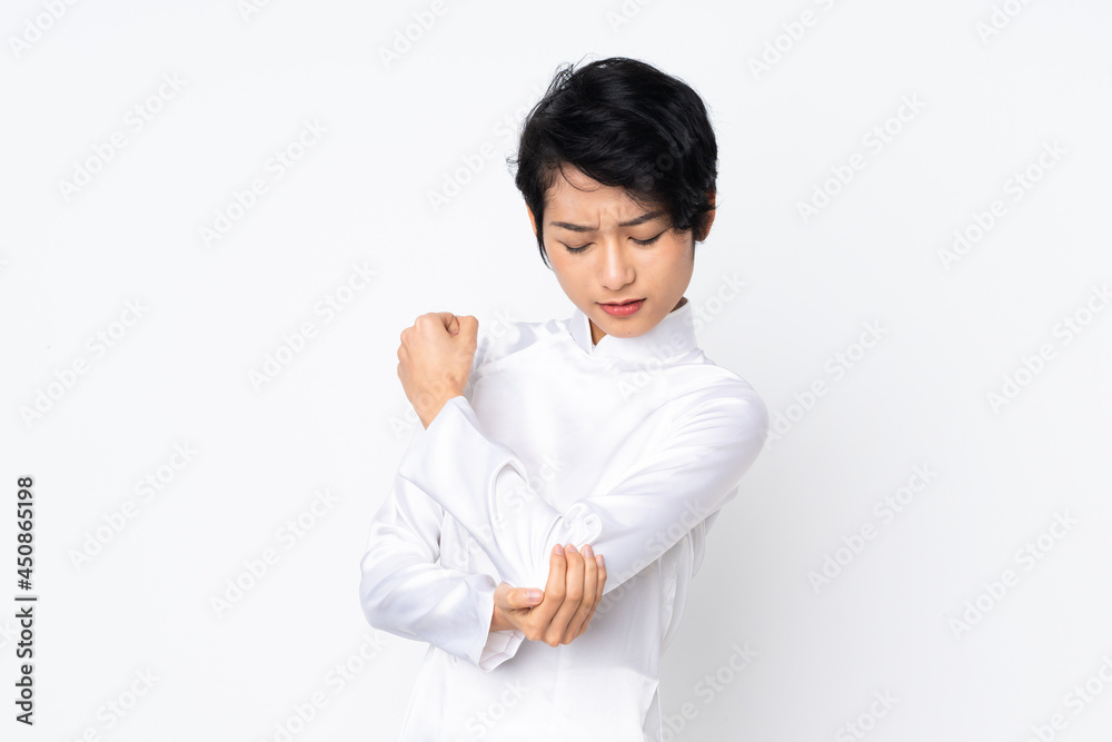 Young Vietnamese woman with short hair wearing a traditional dress over isolated white background with pain in elbow Young Vietnamese woman with short hair wearing a traditional dress over isolated white background with pain in elbow