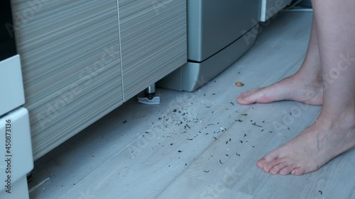 Woman cooks standing on the dirty floor in the kitchen, barefooted feet closeup. Leftovers and crumbs on the kitchen floor. Housekeeping, housework, household duties, cleaning the house concept. photo