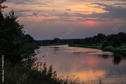 A beautiful landscape - a dramatic sunset sky and a river with reflection and banks with silhouettes of grass and trees and a space to copy