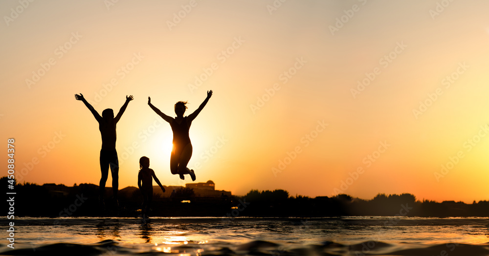Happy family is having fun and jumps at sunset beach in sunlight