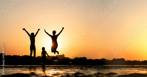 Happy family is having fun and jumps at sunset beach in sunlight