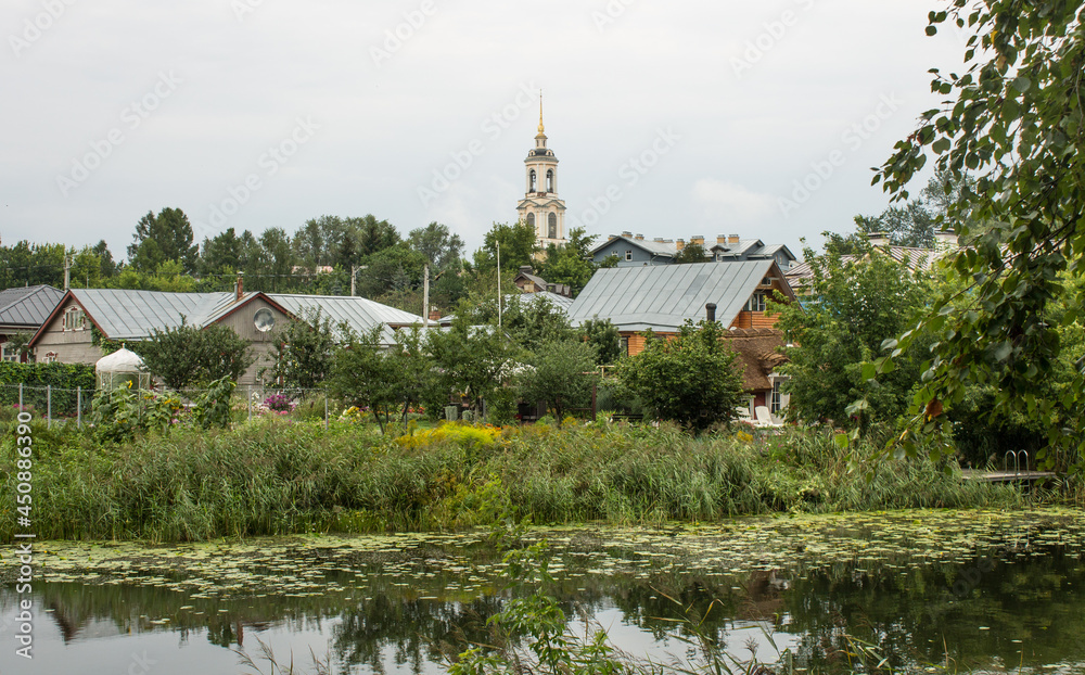 panoramic view of the old town with historical wooden houses and an Orthodox church among the green foliage of trees on the river bank with a reflection on a cloudy day in Suzdal Russia panoramic view of the old town with historical wooden houses and an Orthodox church among the green foliage of trees on the river bank with a reflection on a cloudy day in Suzdal Russia
