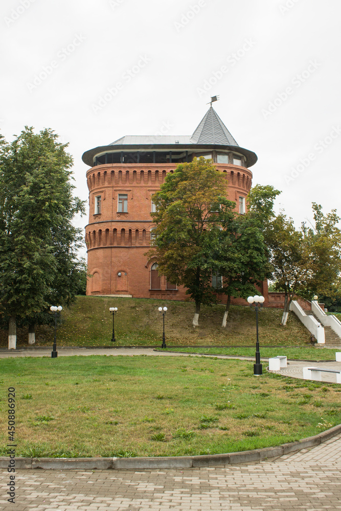 SUZDAL, VLADIMIR REGION, RUSSIA-AUGUST, 11, 2021: Museum-brick water tower and green trees in the old town on a cloudy summer day