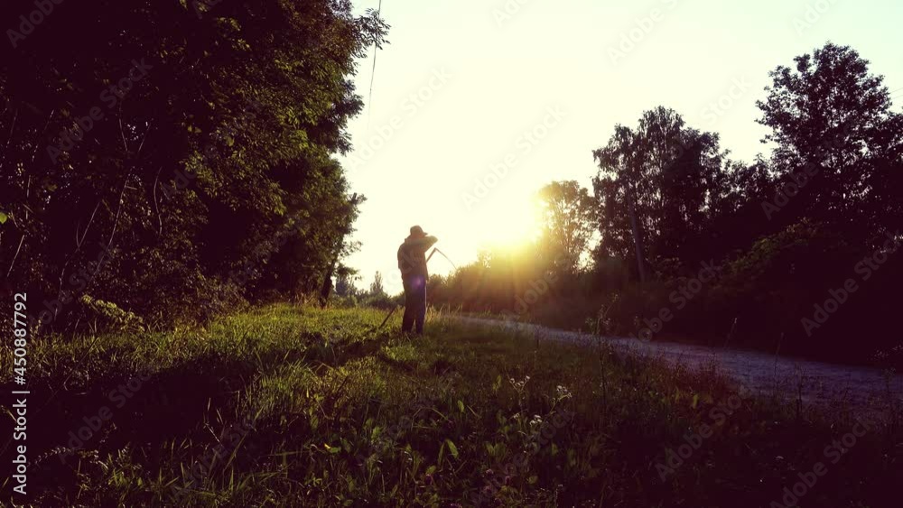 A man mows the grass with a hand scythe, silhouette. A man mows the grass with a hand scythe, silhouette.