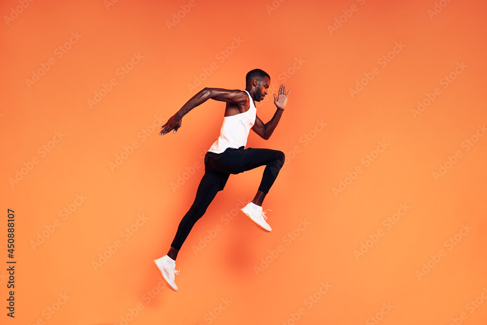 Male runner doing fitness workout. Athlete exercising over an orange background.