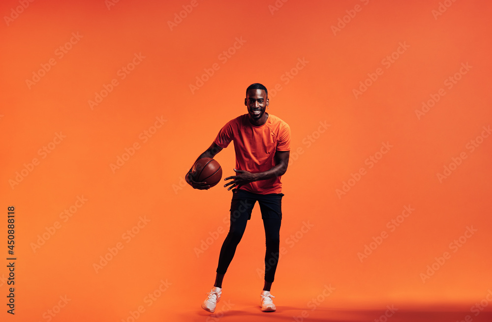 Young smiling man dribbling a basket ball over an orange background in studio