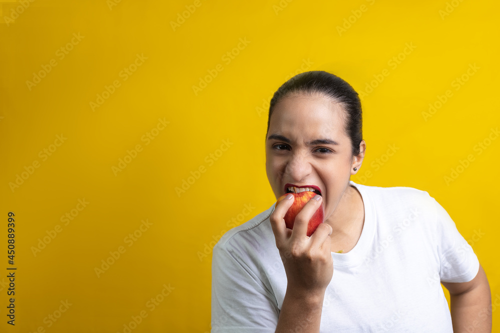 Hispanic woman biting red apple, on yellow background Hispanic woman biting red apple, on yellow background