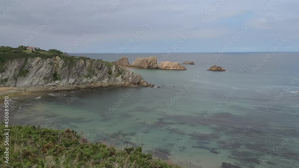 Playa de Arnía en la costa quebrada de Cantabria y tómbolo de arena formado entre la costa y la isla del Castro durante la marea baja, España