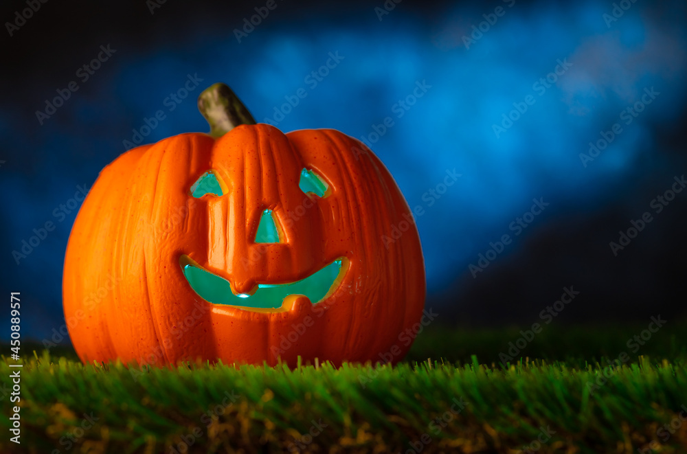 Halloween background. An orange pumpkin in the form of a head on green grass against the background of a dark cloudy night sky. Greeting card, invitation, advertisement, banner, poster. Halloween background. An orange pumpkin in the form of a head on green grass against the background of a dark cloudy night sky. Greeting card, invitation, advertisement, banner, poster.