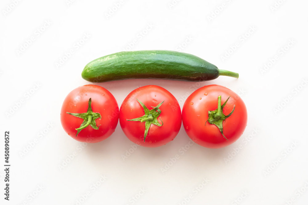 Three red ripe tomatoes with one green cucumber above them Three red ripe tomatoes with one green cucumber above them